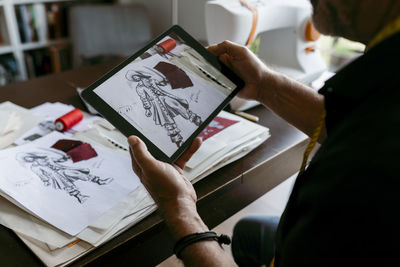 Male tailor photographing sketch through digital tablet at work studio