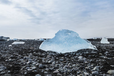 Close-up of ice over pebble stones against sky