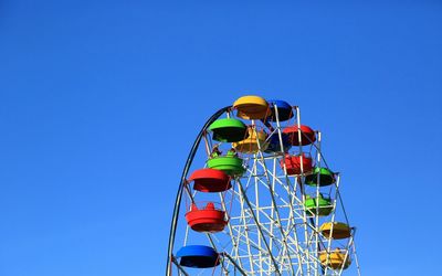 Low angle view of multi colored ferris wheel against clear blue sky