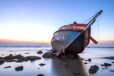 Abandoned boat on beach against sky during sunset