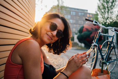 Portrait of smiling woman using mobile phone while sitting outdoors