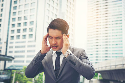 Tensed businessman with head in hands standing against buildings in city 