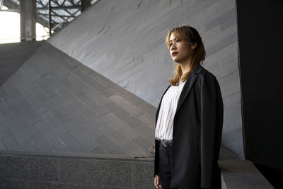 Businesswoman looking away while standing against wall