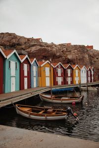 Boats moored in lake by houses against sky