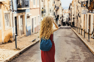 Rear view of woman with backpack walking on road amidst buildings