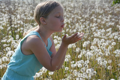 Side view of girl blowing dandelion seeds on field