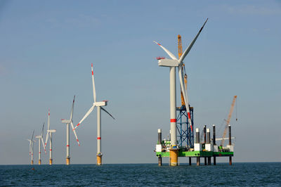 Wind turbines in sea against clear sky