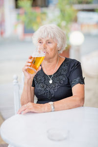 Mature woman sitting at a table in a summer cafe and drinking beer