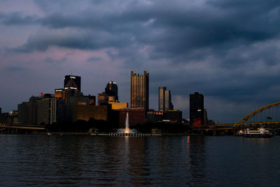 View of city at waterfront against cloudy sky