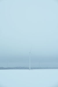 Wind turbines on snow covered landscape against sky