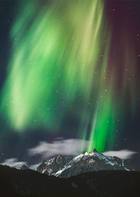 Aurora polaris over snowcapped mountains against sky at night