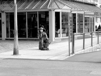 Man sitting on street against building in city