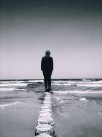 Teenage boy standing at beach against sky