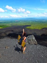 Woman pointing while standing on land against cloudy sky