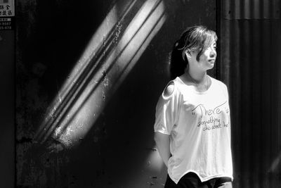 Young woman looking away while standing against wall