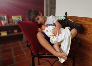 Portrait of boy sitting with newborn sibling on chair at home