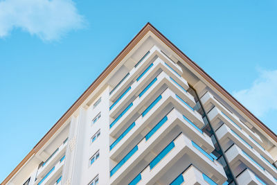 Corner of a residential apartment building with balconies against the blue sky.