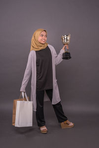 Portrait of smiling woman standing against gray background
