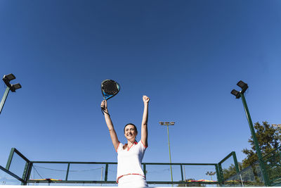 Happy woman cheering at sports court on sunny day