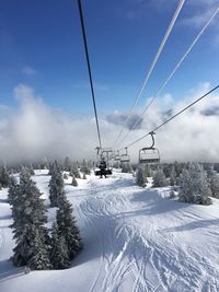 Ski lift over snowy field against sky on sunny day