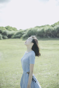 Beautiful woman looking up while standing on field against clear sky