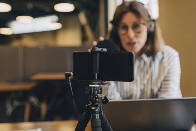 Smart phone on tripod filming businesswoman with laptop in office