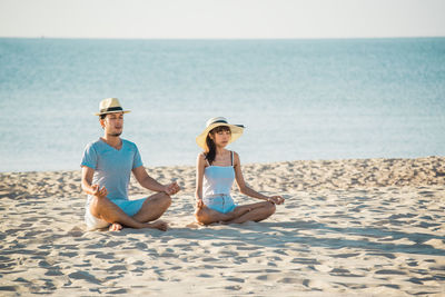 Friends sitting on shore at beach against sky