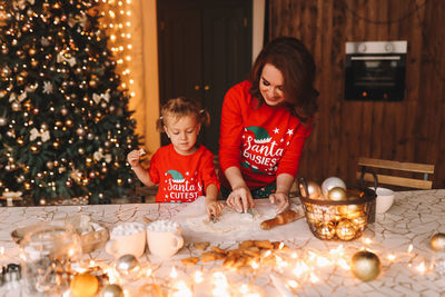 Cheerful parents and a child in red pajamas prepare christmas cookies in the decorated kitchen