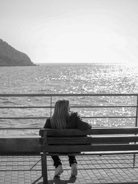 Rear view of woman sitting on bench looking at sea