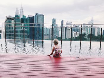 Full length of woman sitting at observation point against cityscape