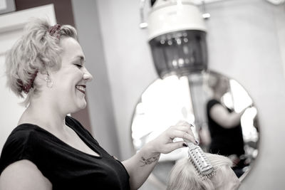 Cheerful female hairdresser styling customer hair in salon