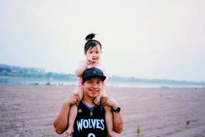 Family portrait of smiling young man and daughter on beach