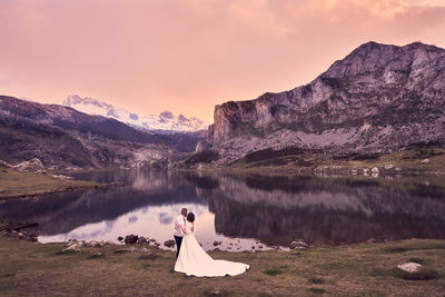 Woman on lake by mountain against sky during sunset