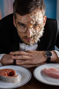 The man chooses between chicken and fish. the man's face is covered with feathers and fish scales.
