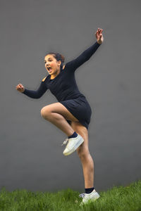 Girl jumping over field against wall