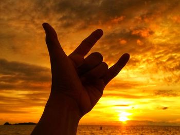 Cropped hand gesturing horn sign against sky during sunset
