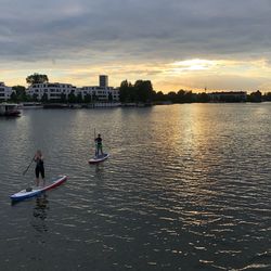 People in river against sky during sunset