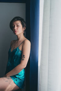 Portrait of young woman standing against wall at home