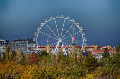 Ferris wheel by buildings against blue sky