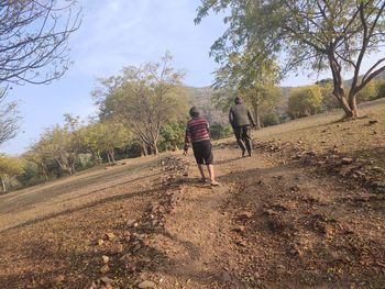 Rear view of people walking on street amidst trees against sky