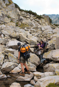 Man and woman with backpacks at stream flowing through rocks