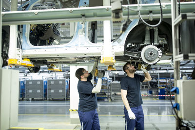 Two colleagues working at car underbody in modern factory