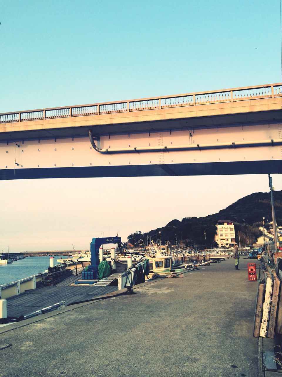 clear sky, built structure, transportation, architecture, copy space, building exterior, road, mode of transport, sea, water, bridge - man made structure, connection, street, beach, outdoors, day, blue, railing, car, incidental people