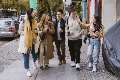 Multiracial male and female friends communicating while walking on sidewalk