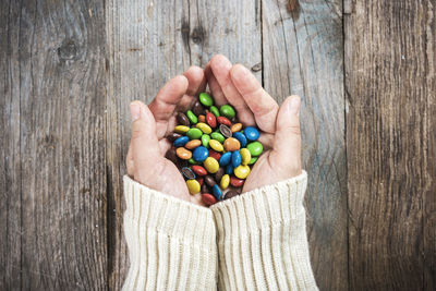 Close-up of colorful round candies in hands of woman on wooden background. top view