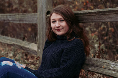 Portrait of smiling girl sitting by wooden railing during autumn