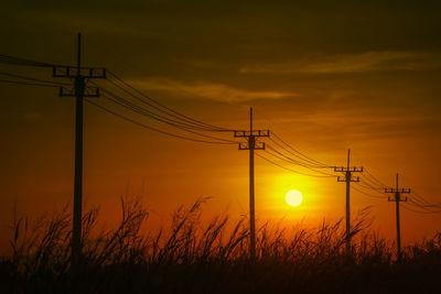 Silhouette electricity pylons on field against romantic sky at sunset