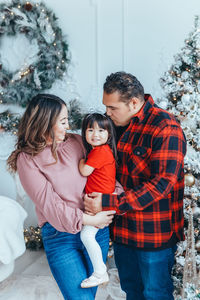 Cheerful parents with daughter by christmas tree at home