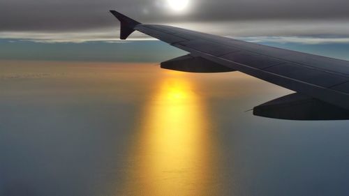 Airplane wing over sea against sky during sunset