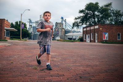 Portrait of boy running on street against cloudy sky